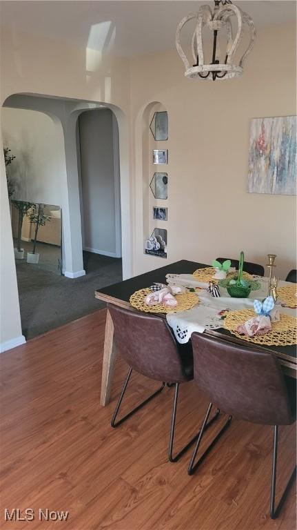 dining area featuring an inviting chandelier, wood finished floors, arched walkways, and baseboards