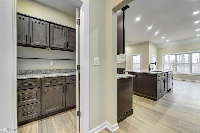 kitchen with dark brown cabinetry, a stone fireplace, recessed lighting, light wood-style floors, and a sink