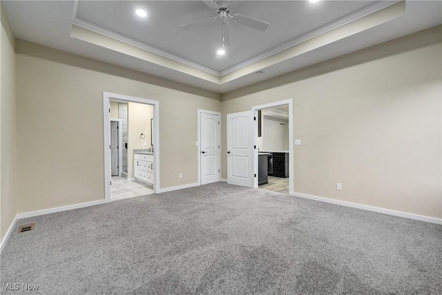 unfurnished bedroom featuring visible vents, ornamental molding, a tray ceiling, connected bathroom, and light colored carpet