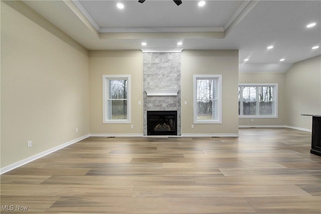 unfurnished living room featuring a stone fireplace, a raised ceiling, a ceiling fan, and wood finished floors