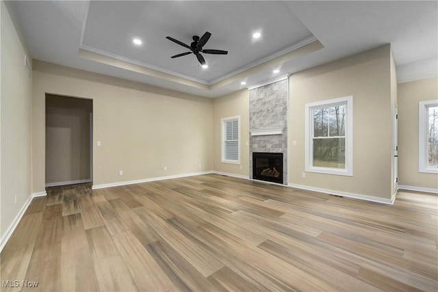 unfurnished living room with baseboards, light wood-type flooring, a fireplace, a raised ceiling, and a ceiling fan