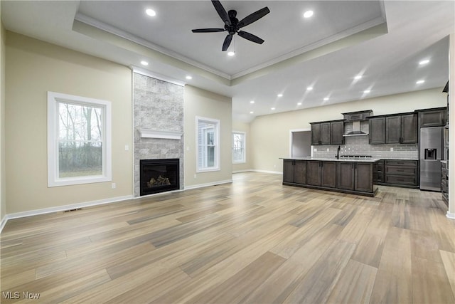 kitchen with a raised ceiling, open floor plan, stainless steel refrigerator with ice dispenser, and wall chimney range hood