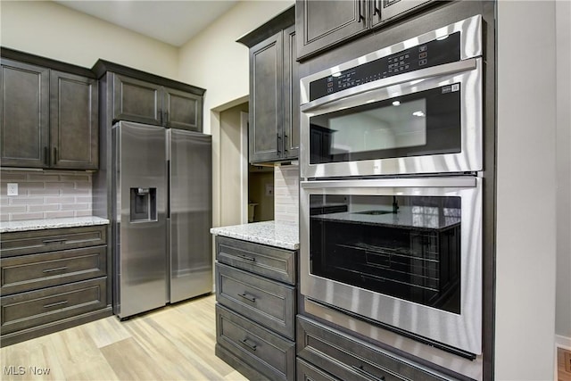 kitchen with decorative backsplash, stainless steel appliances, light wood-style floors, and light stone countertops