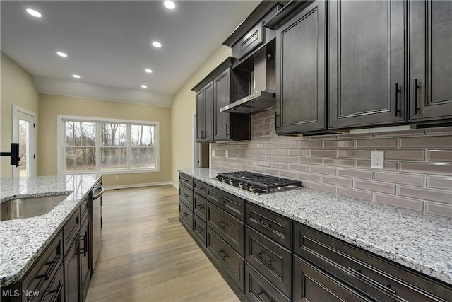 kitchen with backsplash, wall chimney range hood, light wood-style floors, stainless steel appliances, and a sink