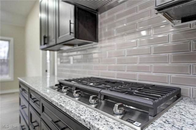 kitchen with backsplash, light stone countertops, gray cabinets, and stainless steel gas stovetop