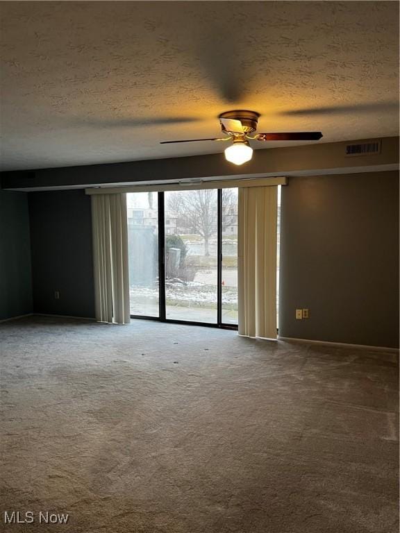 carpeted empty room with visible vents, a textured ceiling, and ceiling fan