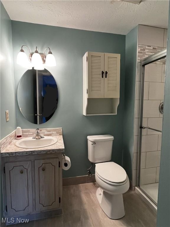 bathroom featuring baseboards, toilet, vanity, and a tile shower