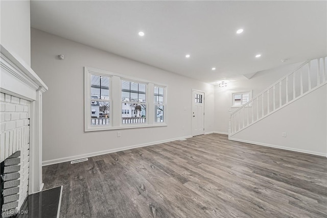 unfurnished living room with wood finished floors, baseboards, recessed lighting, a fireplace, and stairs