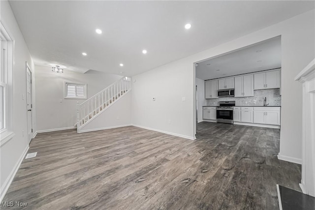 unfurnished living room featuring dark wood-style floors, baseboards, recessed lighting, a sink, and stairs