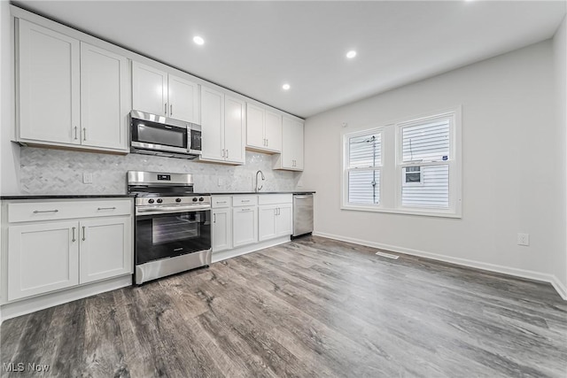 kitchen featuring a sink, tasteful backsplash, wood finished floors, stainless steel appliances, and white cabinets