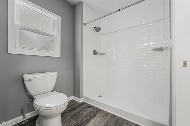 bathroom featuring baseboards, toilet, wood finished floors, and a tile shower