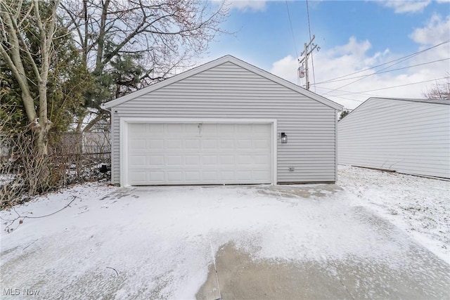 snow covered garage featuring a detached garage and fence