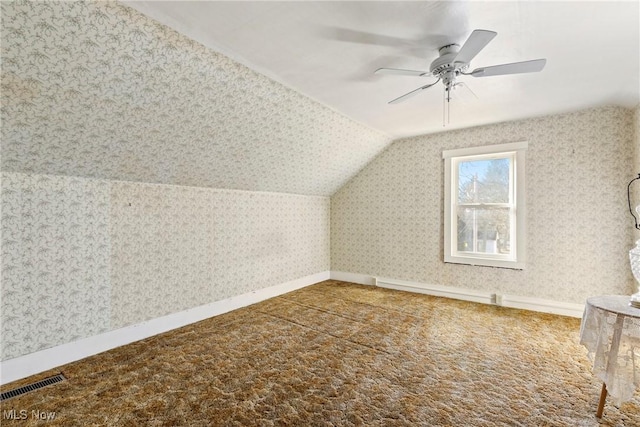 additional living space with carpet, visible vents, baseboards, wallpapered walls, and lofted ceiling