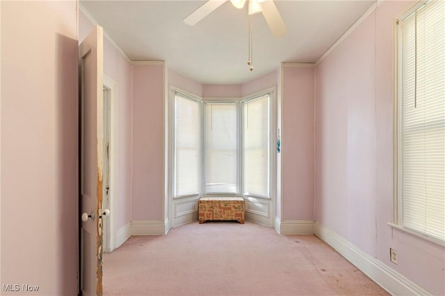 spare room featuring light colored carpet, a ceiling fan, crown molding, and baseboards