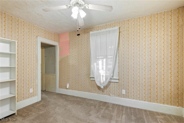 carpeted spare room featuring wallpapered walls, ceiling fan, baseboards, and a textured ceiling