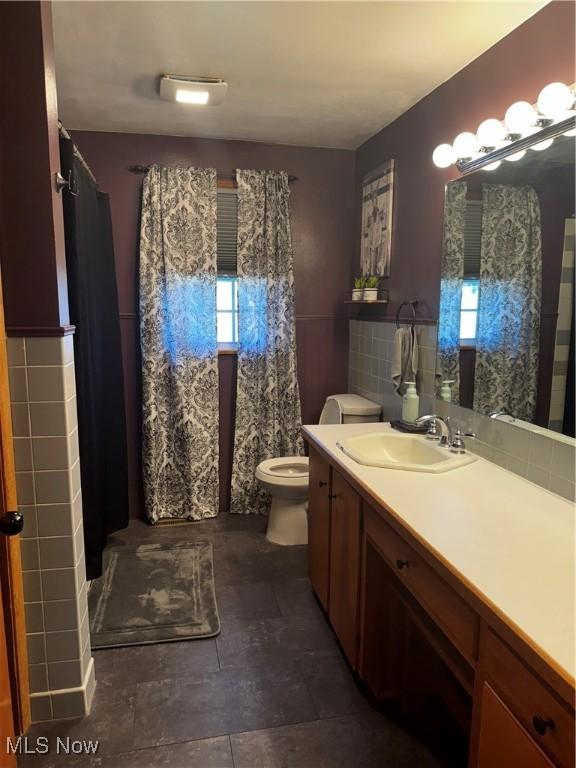 bathroom featuring vanity, tile walls, and toilet