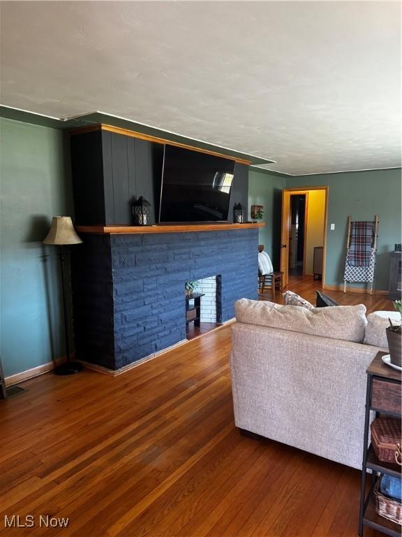 living room with a stone fireplace, wood finished floors, visible vents, and baseboards