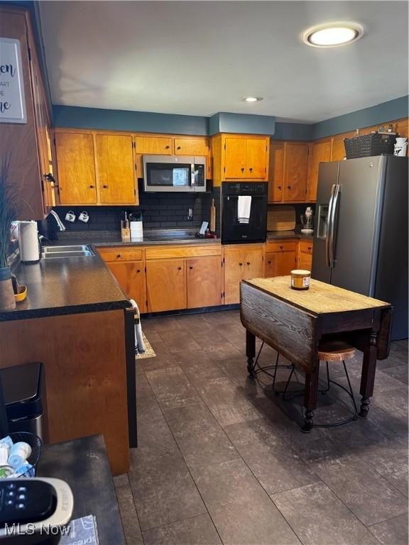 kitchen with black appliances, a sink, backsplash, dark countertops, and brown cabinetry