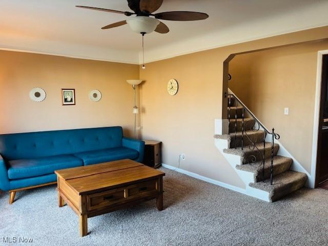 carpeted living room featuring crown molding, stairway, baseboards, and ceiling fan