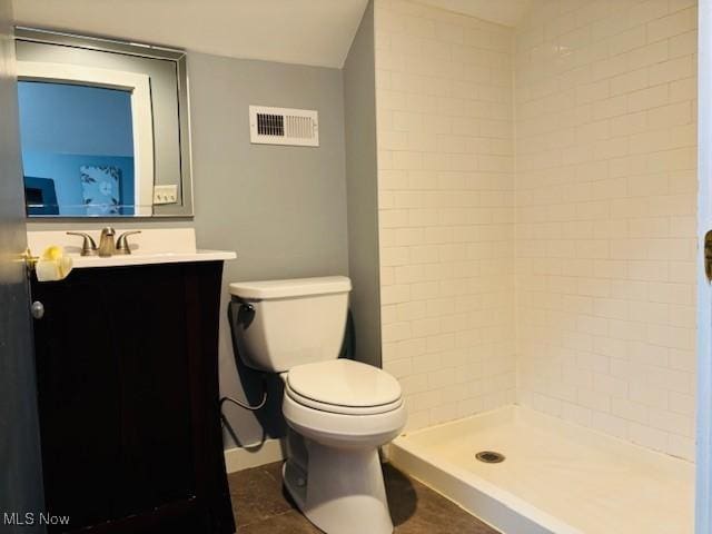 bathroom featuring visible vents, toilet, vanity, and a tile shower