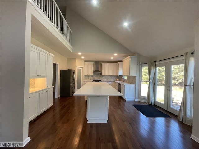 kitchen featuring dark wood-style floors, a kitchen island, light countertops, stainless steel refrigerator with ice dispenser, and wall chimney range hood