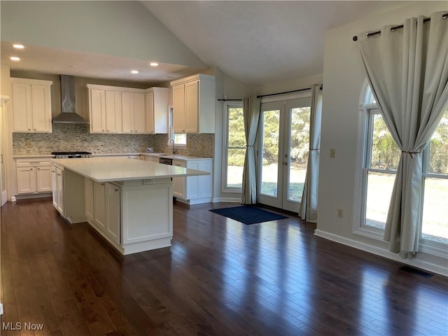 kitchen featuring visible vents, dark wood-type flooring, wall chimney range hood, light countertops, and lofted ceiling