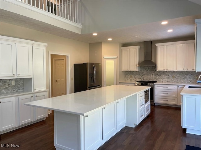 kitchen with a sink, white cabinets, appliances with stainless steel finishes, wall chimney exhaust hood, and a center island