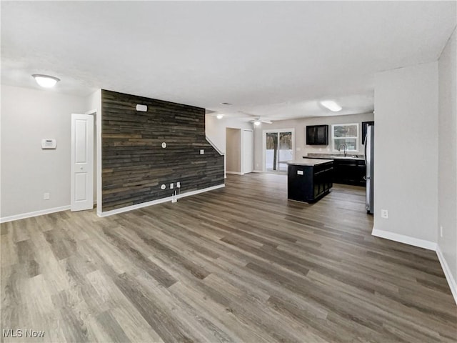 unfurnished living room featuring a sink, baseboards, wooden walls, and wood finished floors