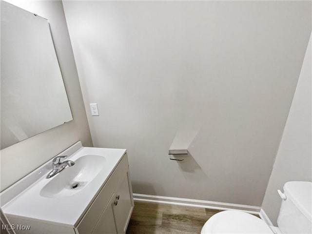 bathroom with toilet, vanity, baseboards, and wood finished floors