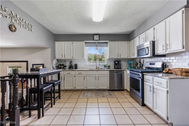 kitchen featuring backsplash, appliances with stainless steel finishes, light tile patterned flooring, white cabinetry, and a sink