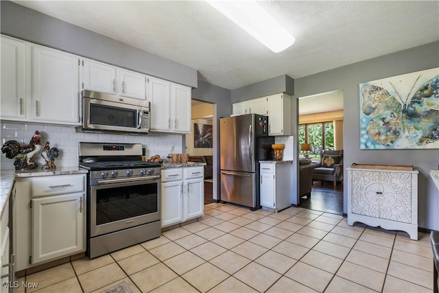 kitchen with tasteful backsplash, appliances with stainless steel finishes, white cabinetry, and light stone countertops