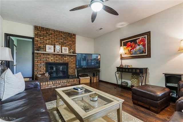 living area featuring visible vents, wood finished floors, baseboards, a brick fireplace, and ceiling fan