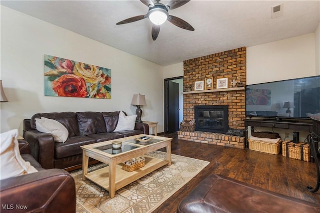 living area featuring a brick fireplace, wood finished floors, and ceiling fan