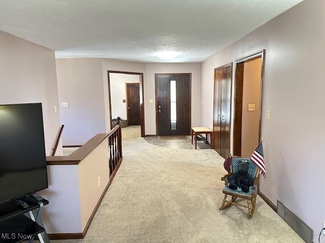 hallway featuring an upstairs landing, visible vents, baseboards, and carpet floors