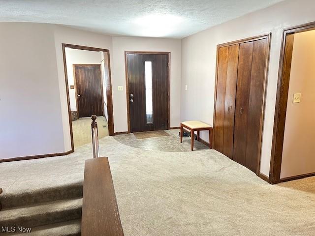 foyer entrance featuring baseboards, light carpet, and a textured ceiling