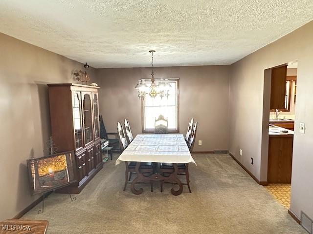 dining room featuring baseboards, a notable chandelier, light carpet, and a textured ceiling