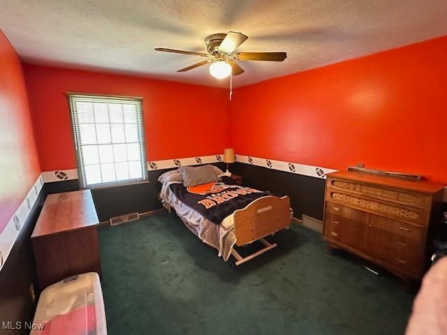 bedroom featuring visible vents, baseboards, ceiling fan, a textured ceiling, and dark colored carpet