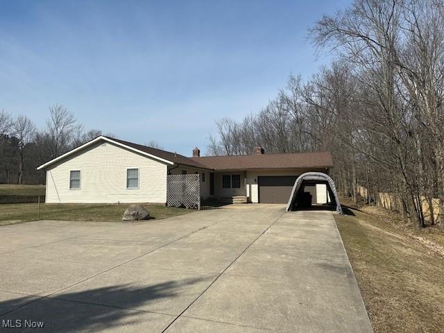 ranch-style house with an attached garage, a chimney, and concrete driveway