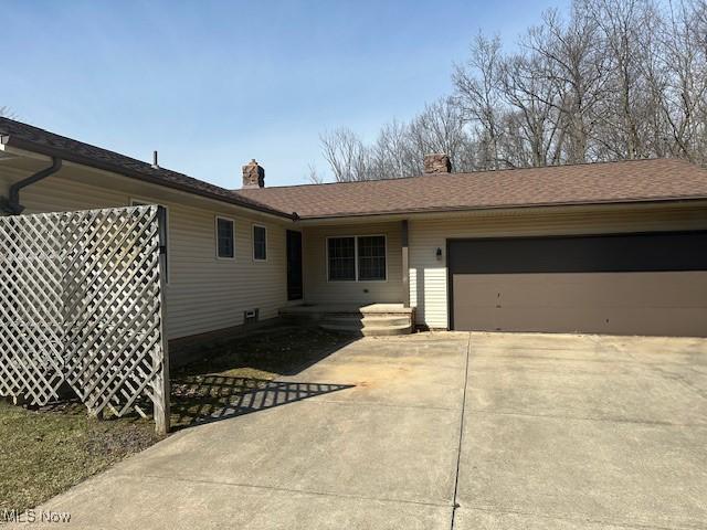 view of front of home featuring concrete driveway, a chimney, and a garage