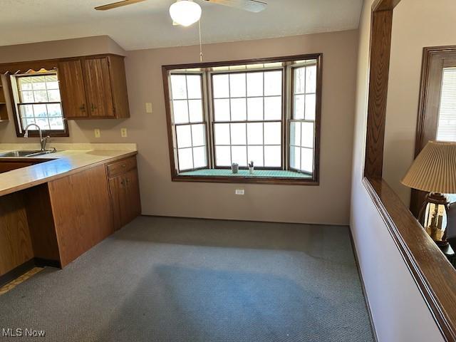 kitchen featuring brown cabinetry, a sink, carpet, and a ceiling fan