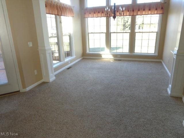 unfurnished room with baseboards, carpet, a healthy amount of sunlight, and ornate columns