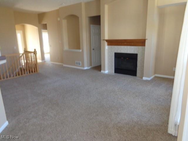 unfurnished living room with a tiled fireplace, baseboards, and carpet floors