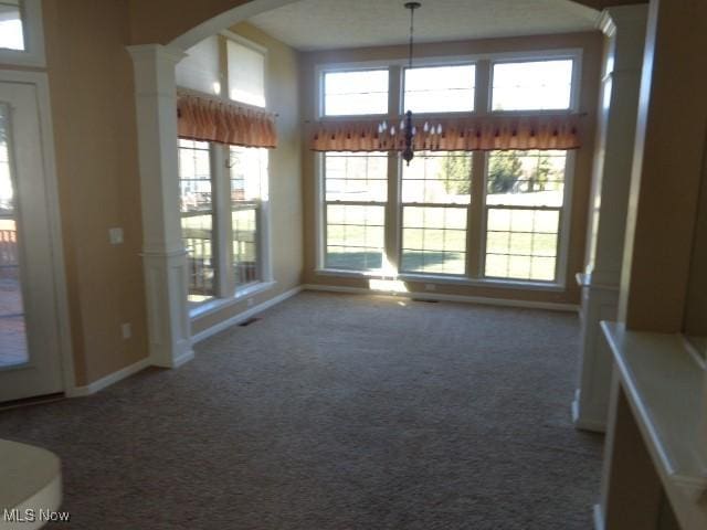 unfurnished dining area featuring baseboards, carpet floors, a high ceiling, decorative columns, and arched walkways