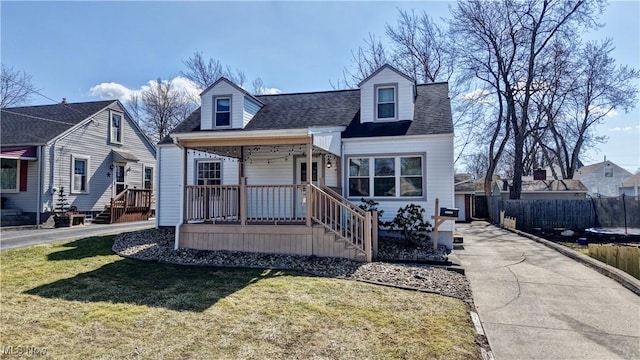 cape cod home featuring a trampoline, a front lawn, fence, roof with shingles, and covered porch