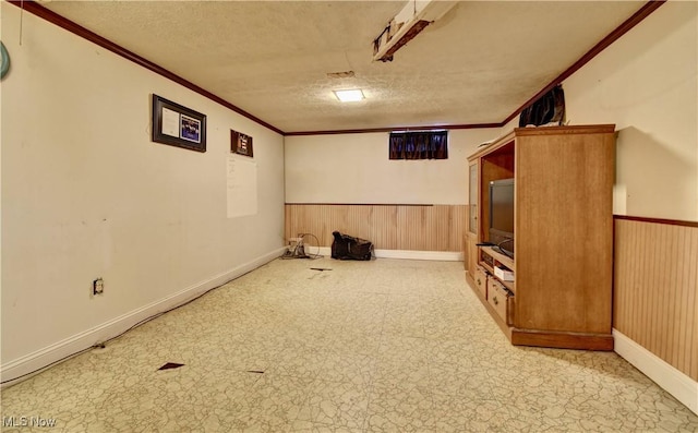 finished basement featuring a textured ceiling, ornamental molding, wainscoting, and wood walls