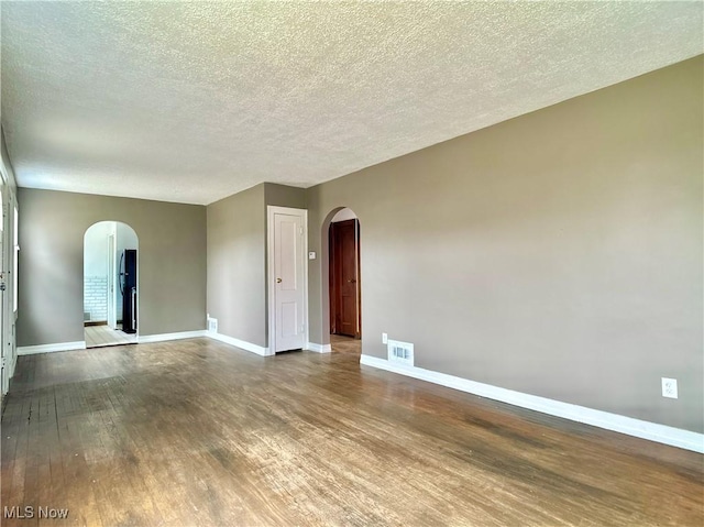 empty room featuring wood finished floors, visible vents, arched walkways, and baseboards