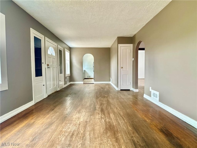 foyer featuring visible vents, arched walkways, baseboards, and wood finished floors