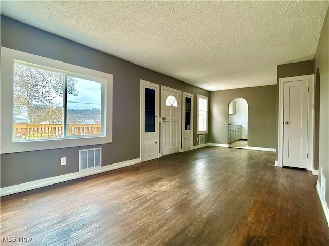 entrance foyer with visible vents, baseboards, arched walkways, dark wood-style flooring, and a textured ceiling