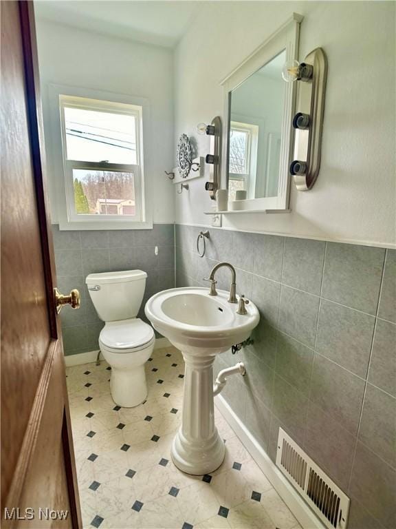 half bathroom featuring visible vents, a wainscoted wall, toilet, a sink, and tile walls