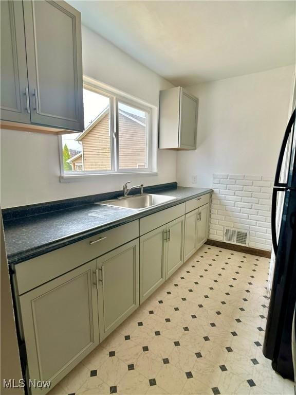 kitchen featuring light floors, visible vents, freestanding refrigerator, a sink, and dark countertops